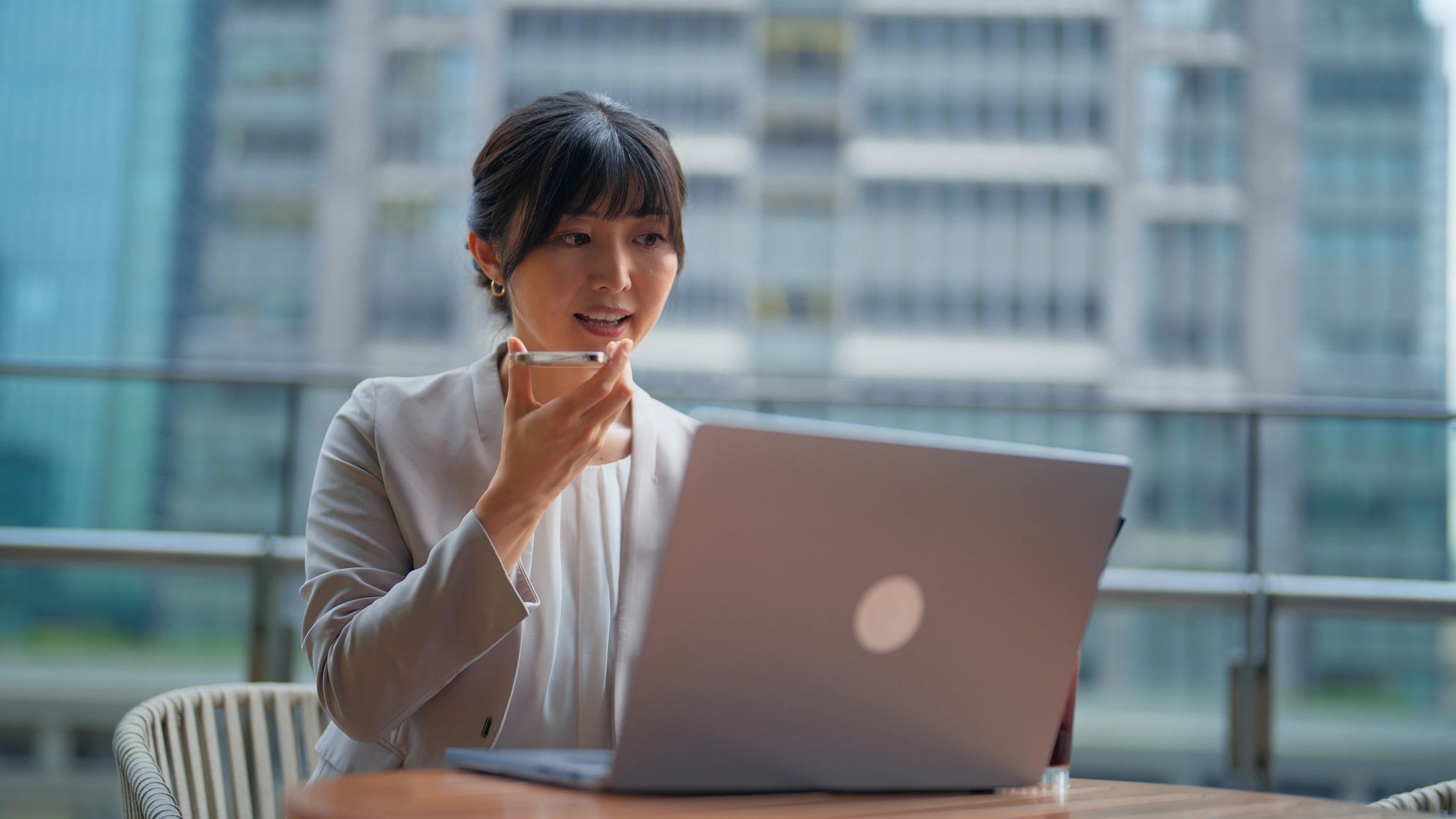 Professional using an AI app on a smartphone while working on a laptop in a business district